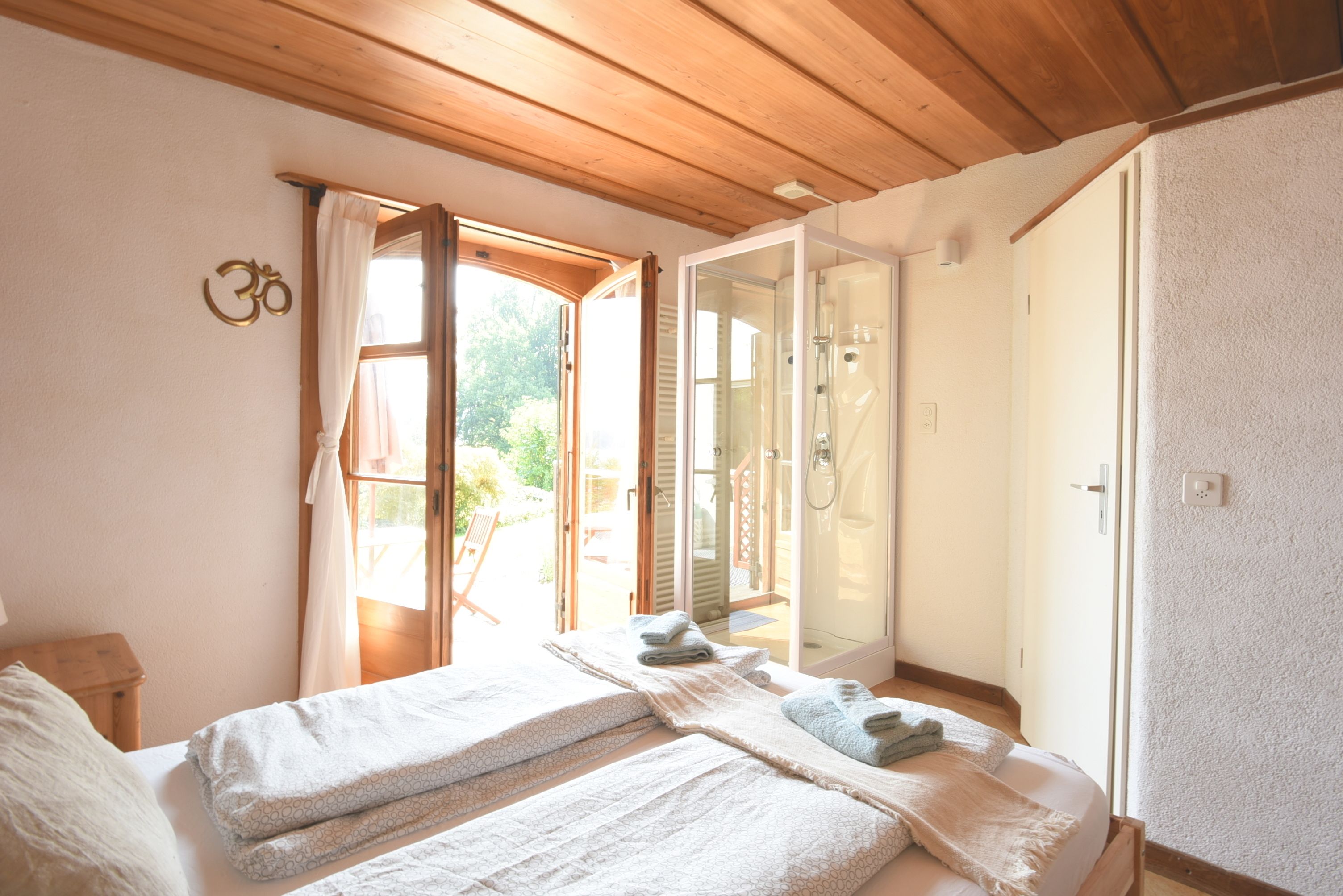 Ein Schlafzimmer mit Holzboden, einem Bett mit zwei Kissen, einer Duschkabine und Blick ins Freie.