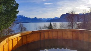 Une terrasse en bois avec un jacuzzi donnant sur un lac et des montagnes.