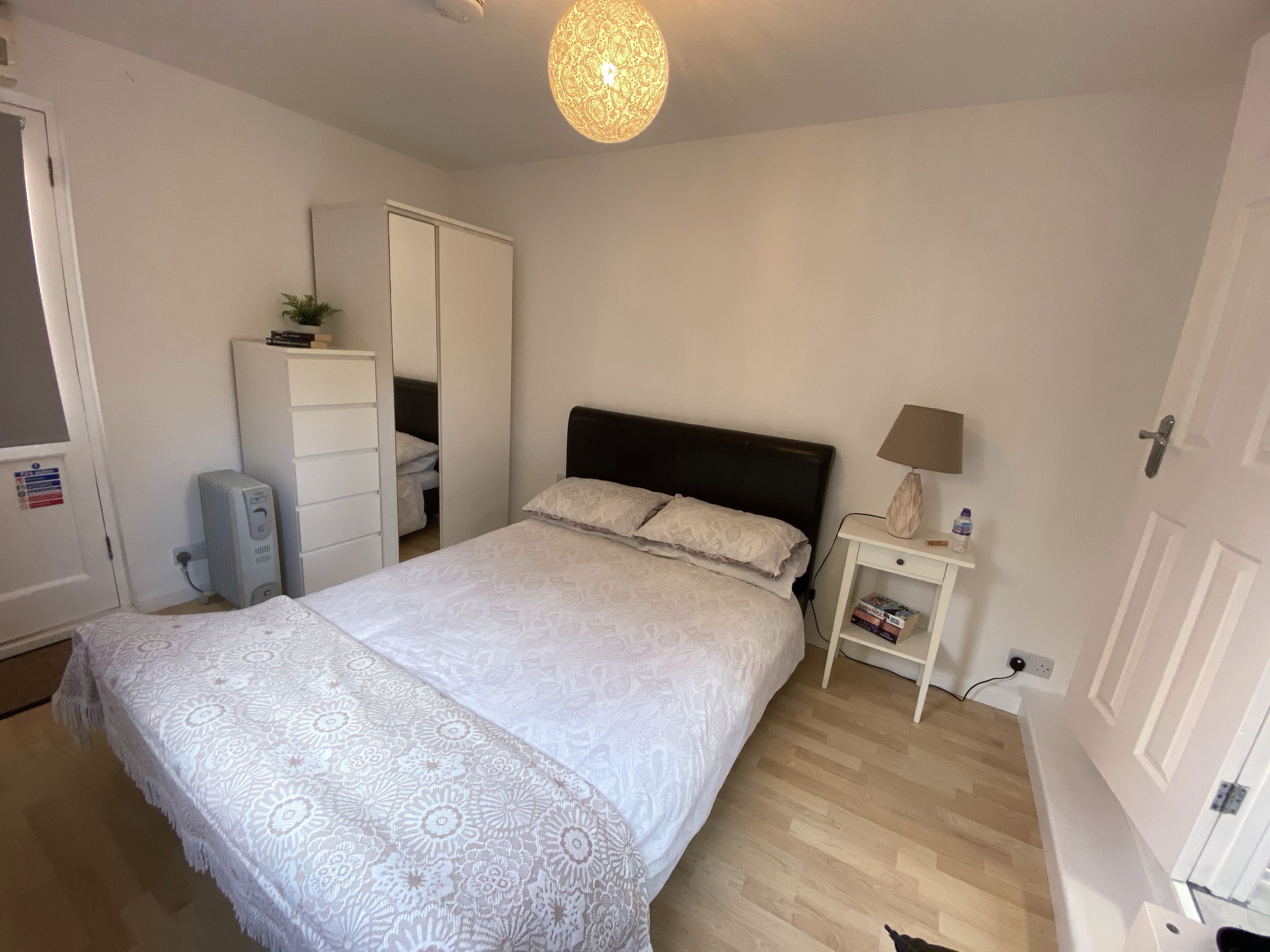 A bedroom with a bed, a nightstand, a lamp, a wardrobe, and a radiator.