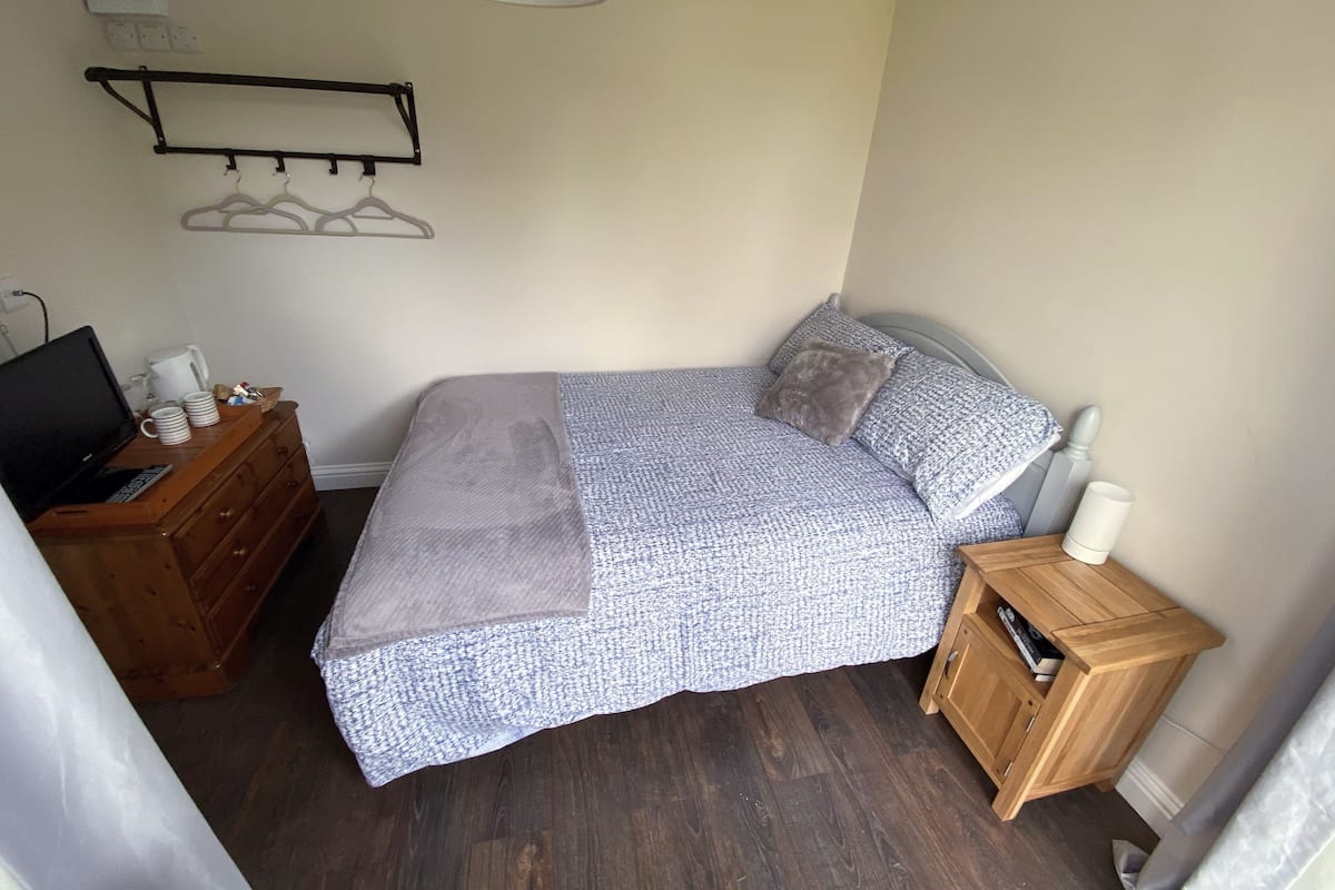 A bedroom with a bed, a wooden dresser, a nightstand, a TV, and a lamp.