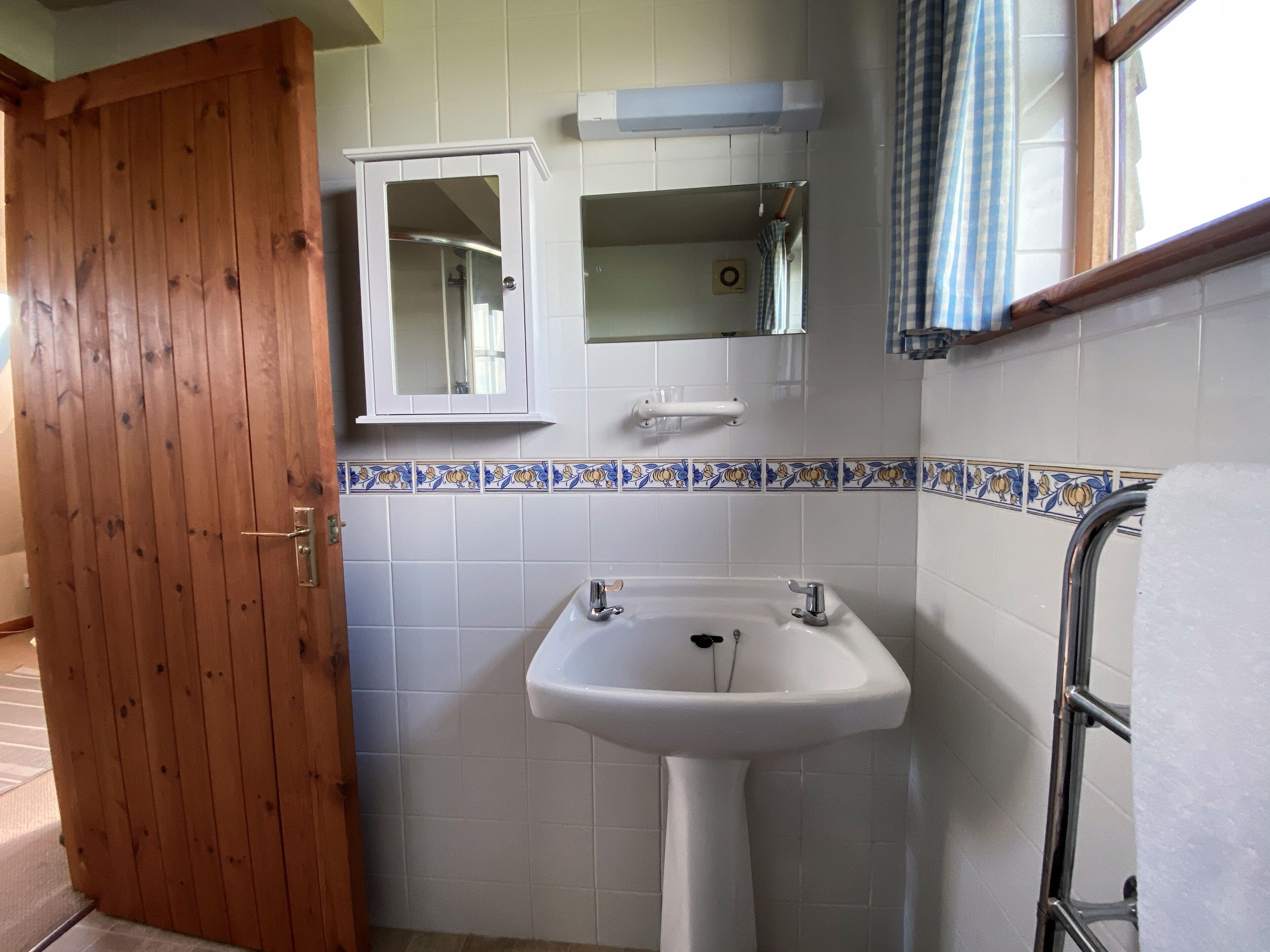 A bathroom with a wooden door, a white sink with two faucets, a mirror, and a towel rack.