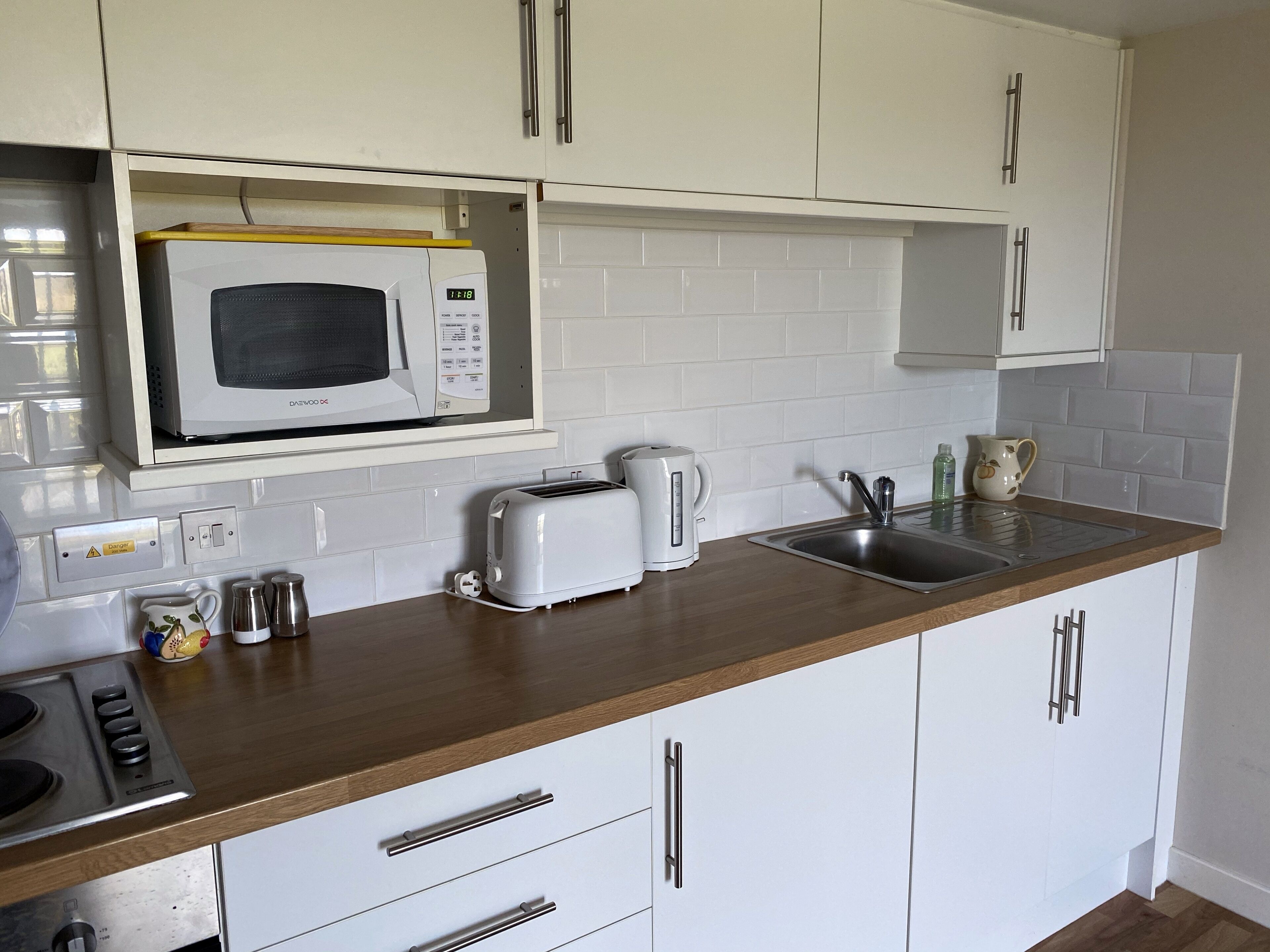 A kitchen with white cabinets, a microwave, a toaster, a kettle, and a sink.
