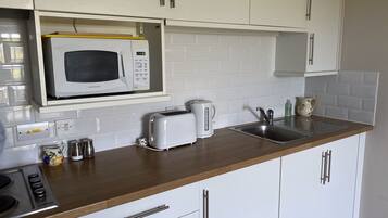 A kitchen with white cabinets, a microwave, a toaster, a kettle, and a sink.