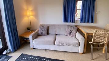 Un salon confortable avec un canapé, une petite table, une lampe et un fauteuil.