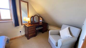 A bedroom with a wooden desk, a chair, a large mirror, and a checkered sofa.