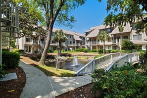 Un patio con un pequeño estanque, un puente y edificios de apartamentos con balcones.