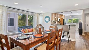A dining area with a wooden table set for four, a kitchen in the background, and a view of greenery outside. - Hilton Head Luxury Condo! Coligny, Dining, Family, Golf - Sleeps 10 
 STR#045066 (Hilton Head Island)