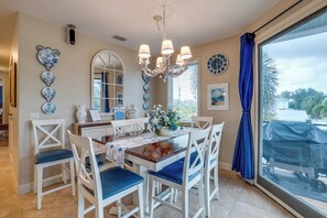 Spiseområde med en lysekrone, hvide stole, et bord med blomsterarrangement og et stort vindue med udsigt.