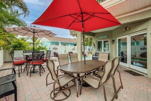 A patio area with a round table and chairs, a red umbrella, and a pool visible through a glass door.