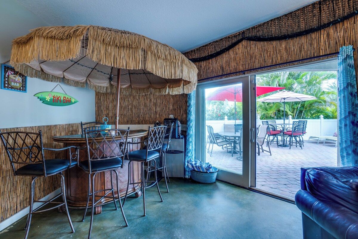 Un espace bar agrémenté d’un parasol en chaume, de tabourets de bar et offrant une vue sur la terrasse extérieure.
