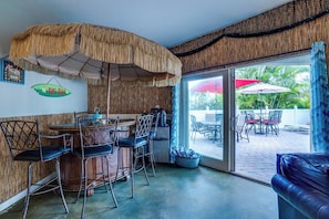 A bar area with a thatched umbrella, bar stools, and a view of the outdoor patio.