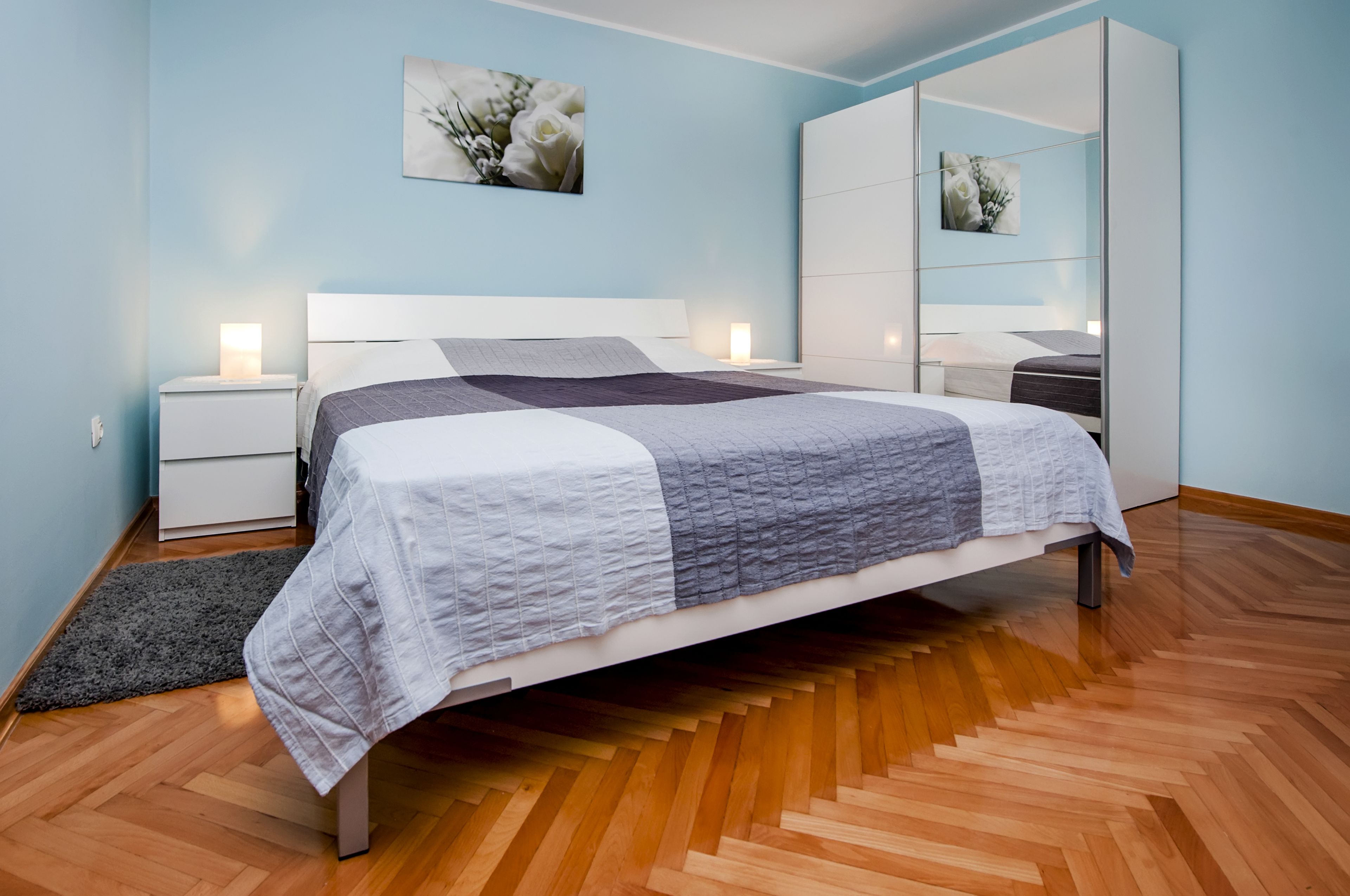 Ein modernes Schlafzimmer mit einem Bett, Nachttischen, einem Schminktisch und einem Holzboden mit Fischgrätmuster.