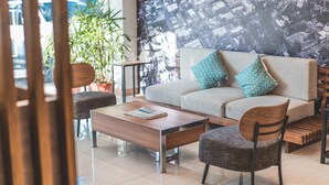 A modern lounge area with a sofa, two armchairs, a wooden coffee table, and a patterned wall. - Henia Hotel (Dumaguete)