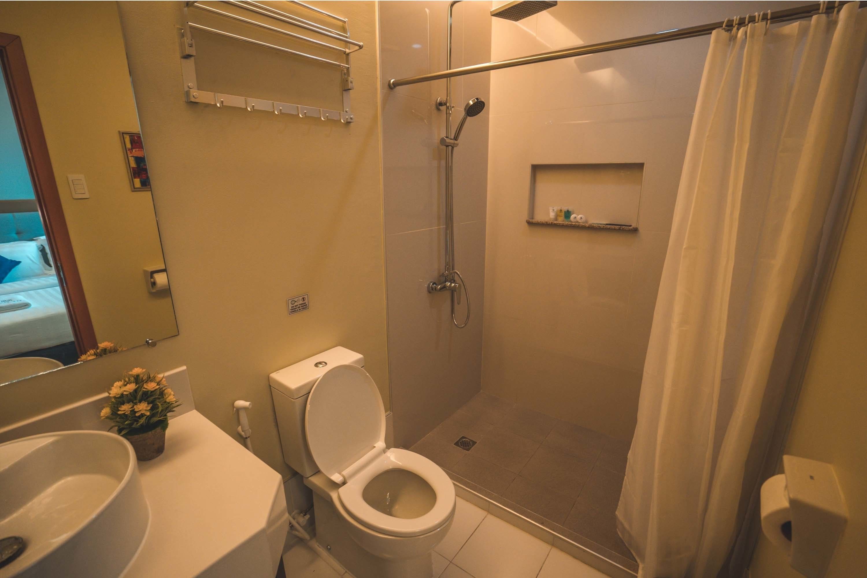 A bathroom with a toilet, sink, shower, and a mirror.