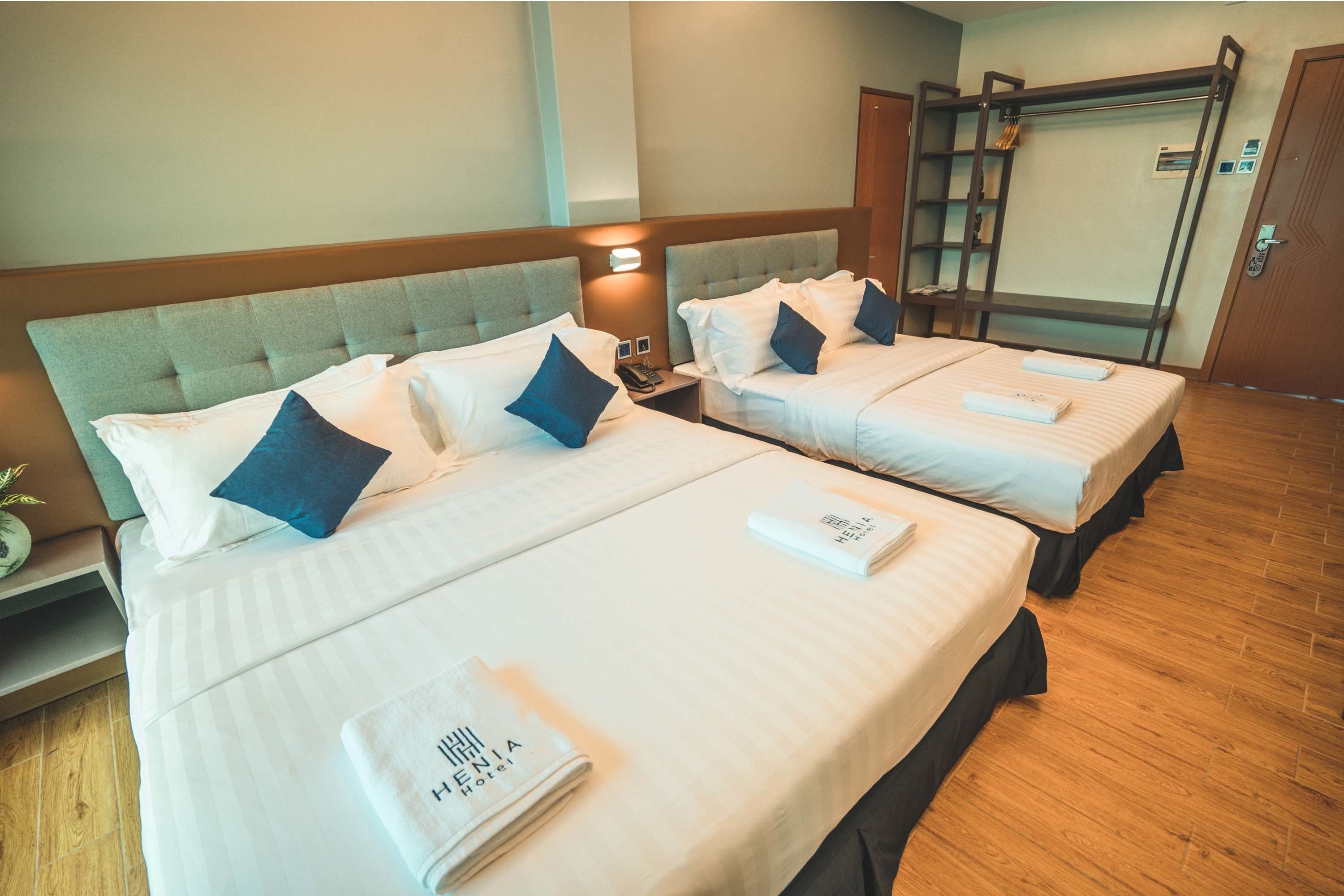 A hotel room with two beds, each with a pillow and a folded towel. There is a bedside table with a lamp and a phone.