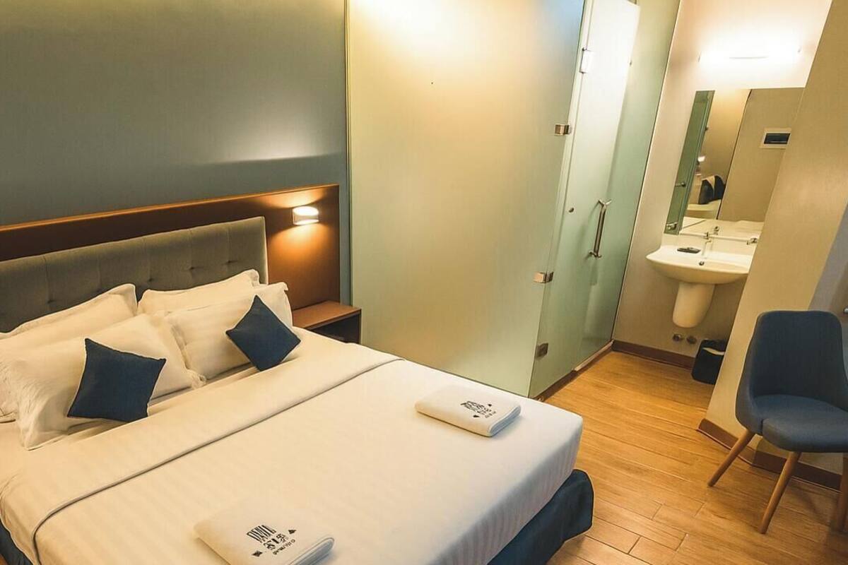 Quarto de hotel com uma cama, mesas de cabeceira, uma cadeira e banheiro com pia e espelho.