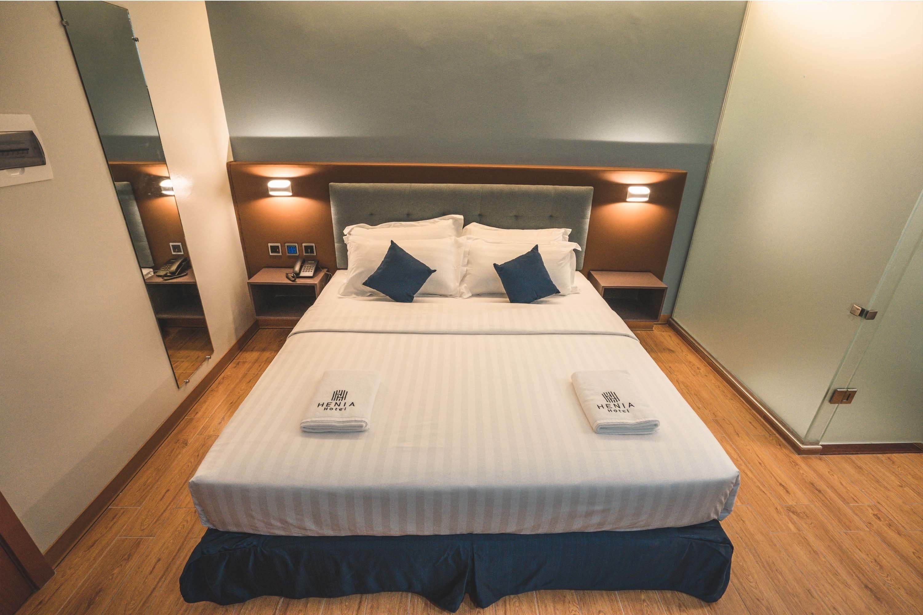 A neatly made bed with a striped bedspread, two pillows, and a folded towel on each side. There are bedside tables with lamps and a telephone on one side.