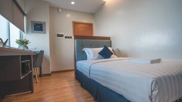 Quarto de hotel com uma cama, uma escrivaninha e uma cadeira.