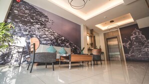 A modern lobby with a high ceiling, a large mural, a reception desk, seating area, and an elevator. - Henia Hotel (Dumaguete)