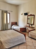 Un dormitorio con dos camas individuales, cabecero de madera, mesita de noche con lámpara, espejo y ventana con cortinas.