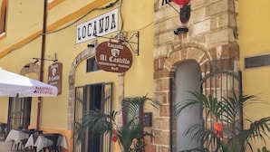 Un edificio amarillo con un letrero que dice "Locanda Al Castello" y "Albero". Hay mesas y sillas afuera, plantas en macetas y un felpudo con el nombre del establecimiento.