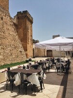 Un espacio de comedor al aire libre con mesas, sillas y un paraguas grande, junto a una pared de piedra.