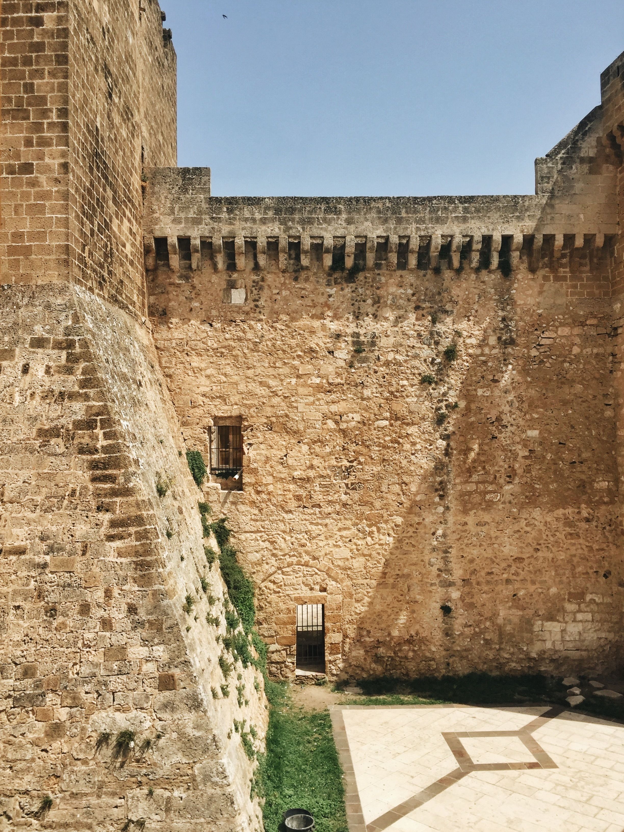 A courtyard with a stone wall, a small window, and a tiled floor.