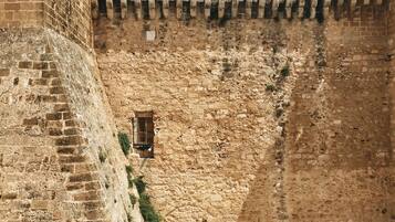 A courtyard with a stone wall, a small window, and a tiled floor.