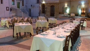 Un área de comedor al aire libre con varias mesas dispuestas para los comensales, con un edificio de piedra de fondo.