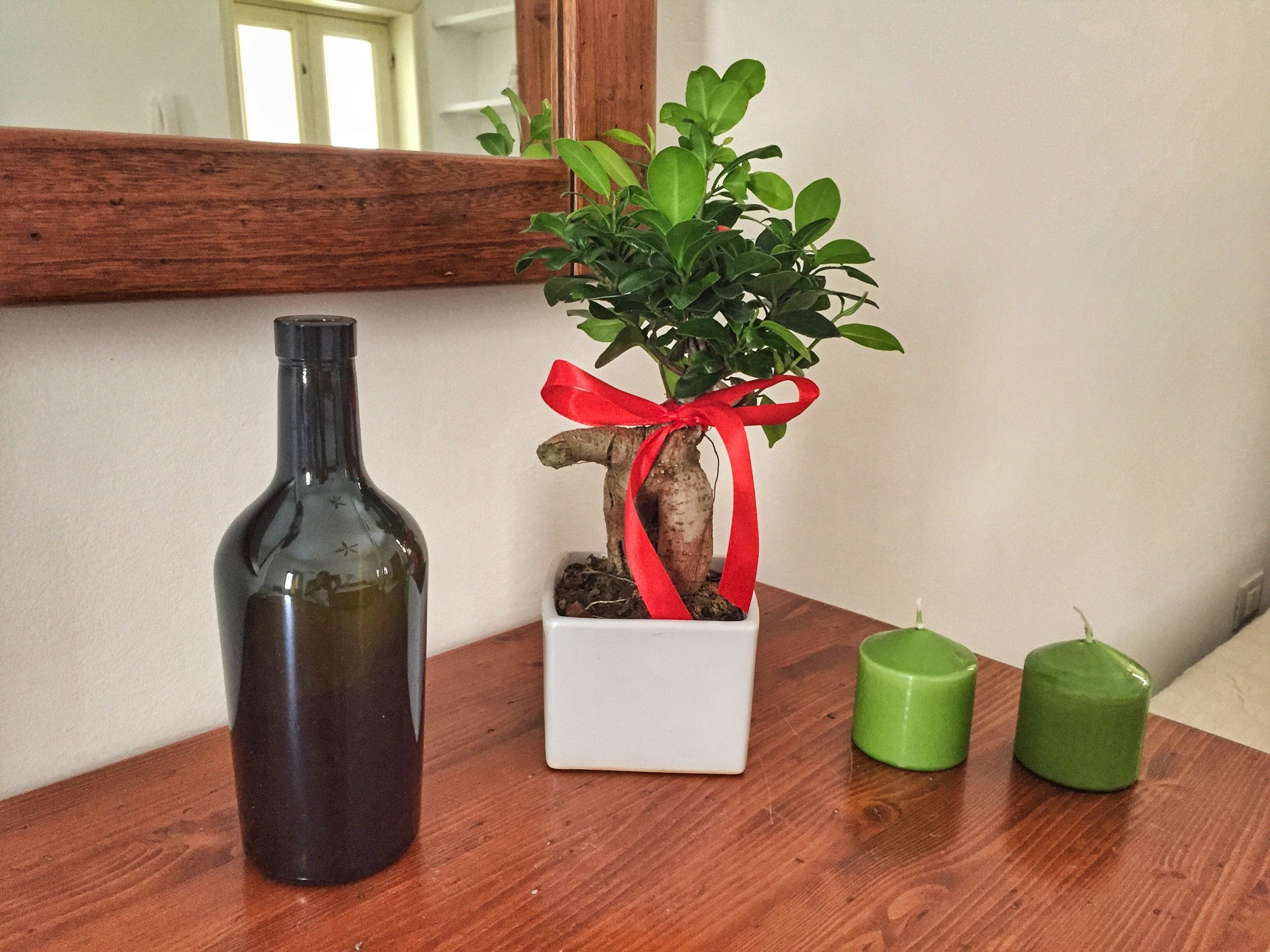A wooden table with a potted plant, a dark bottle, and two green candles.