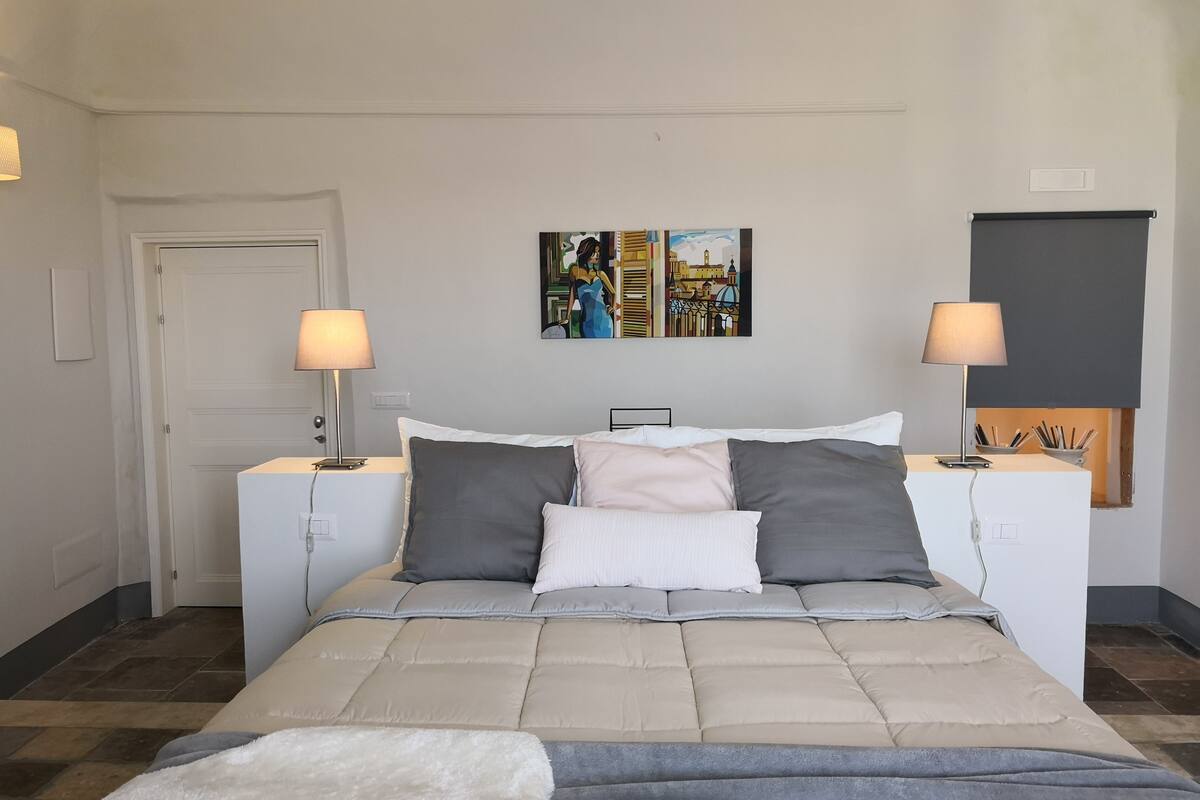 Quarto com cama, duas mesas de cabeceira, duas luminárias, uma porta e uma parede com um quadro.