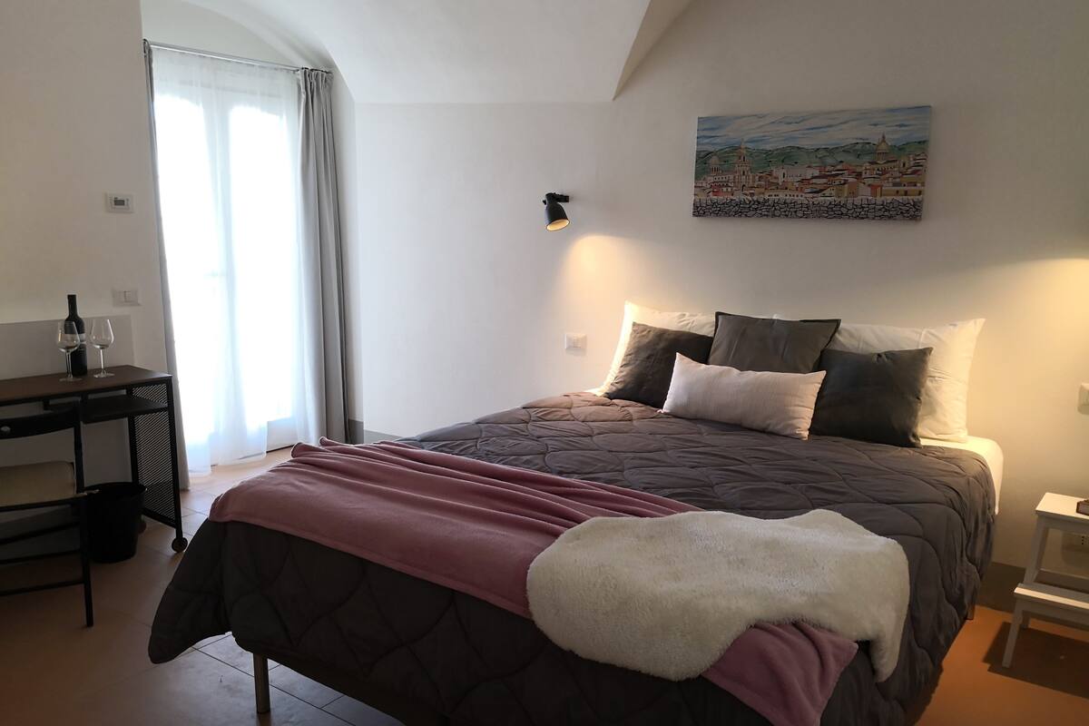 Quarto com cama, escrivaninha e um quadro na parede.
