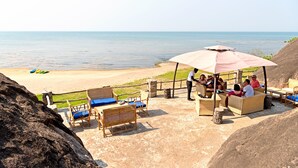 A beachside seating area with wicker furniture and a large umbrella, overlooking the sea. - Safari Beach Lodge (Senga)