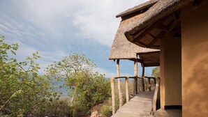 A wooden deck leading to a thatched-roof structure with a view of the surrounding landscape. - Safari Beach Lodge (Senga)
