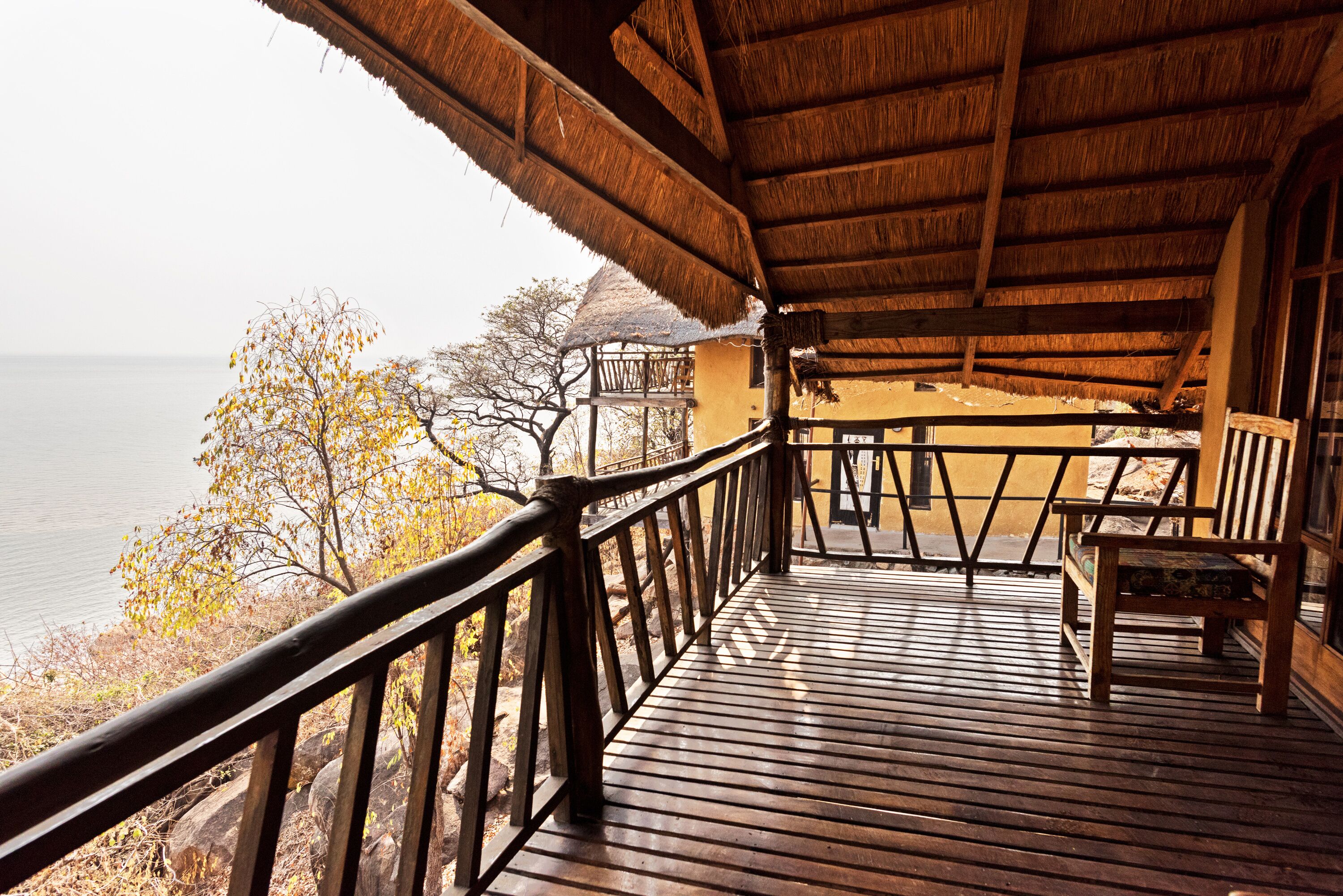 A wooden deck with a thatched roof overlooking a body of water and trees.