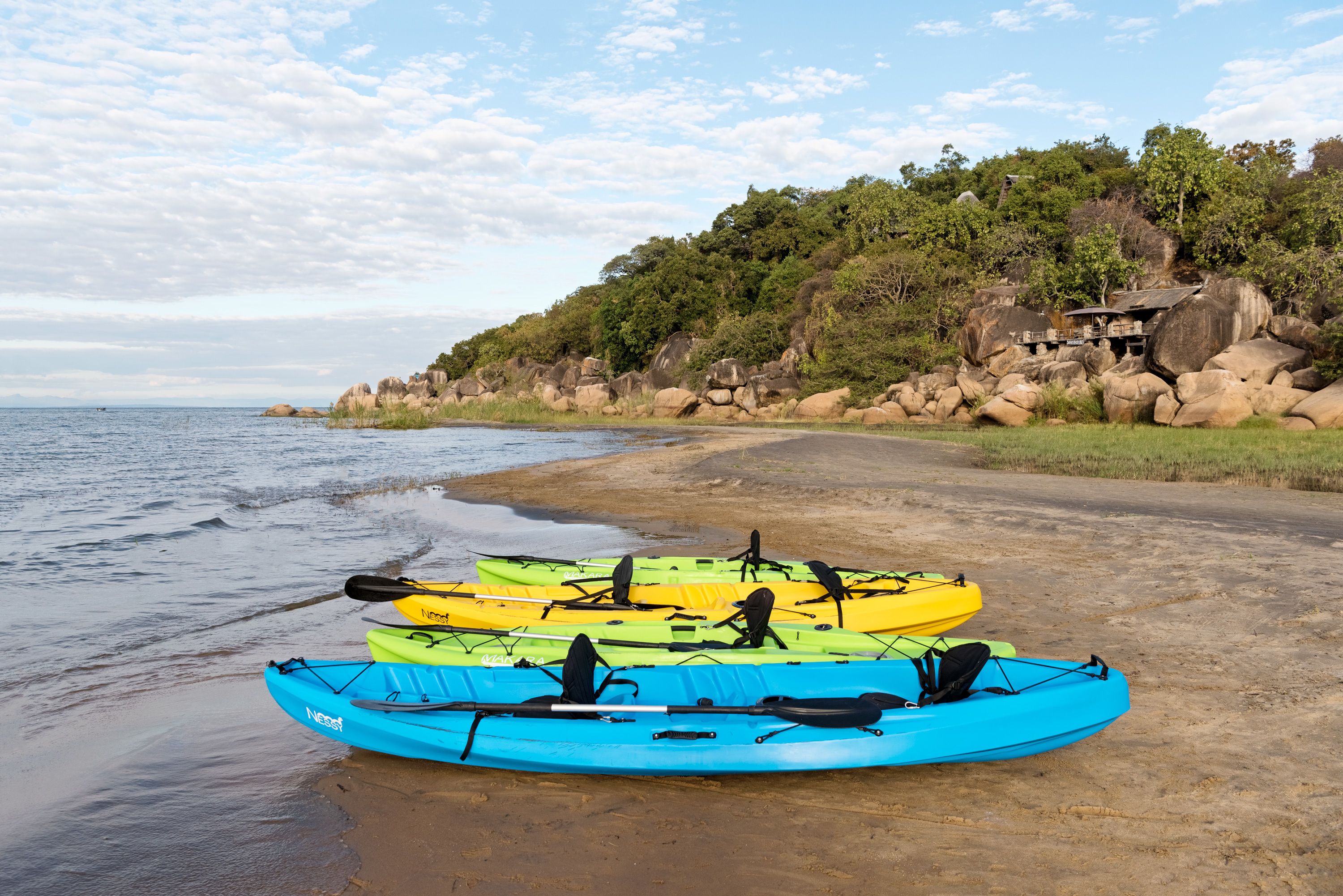 A beach with kayaks lined up on the sand and a rocky hillside in the background.
