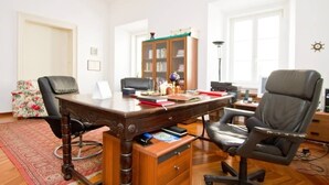 Un escritorio de madera con una computadora, una lámpara y una estantería en una habitación con una alfombra roja y una ventana.