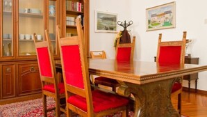 Un comedor con una mesa de madera y sillas tapizadas en rojo. Se observa un mueble de madera con puertas de cristal y un cuadro en la pared.