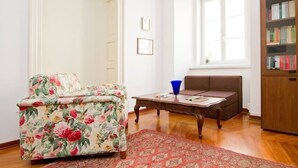 Una sala de estar con un sillón estampado, un sofá marrón, una mesa de centro de madera y una estantería.