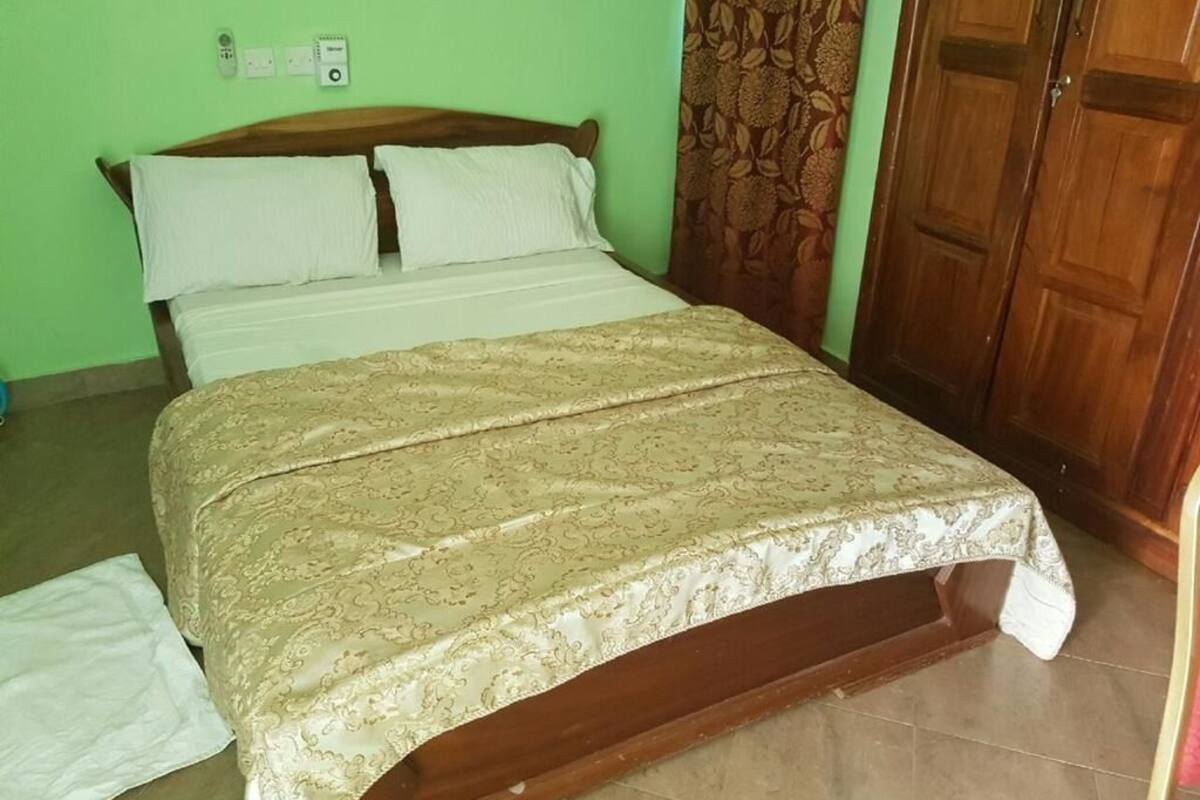 Cama com colcha estampada, cabeceira de madeira e parede verde com tomada.