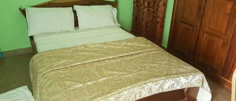 A bed with a patterned bedspread, a wooden headboard, and a green wall with a power outlet.