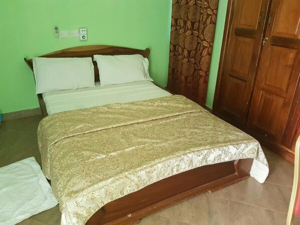 A bed with a patterned bedspread, a wooden headboard, and a green wall with a power outlet. - Blue Hill Hotel (Bamahu)