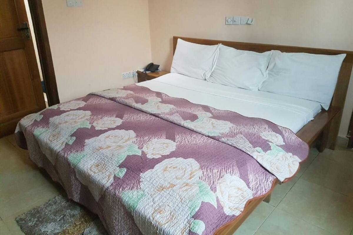 Quarto com cama, mesa de cabeceira e porta de madeira.