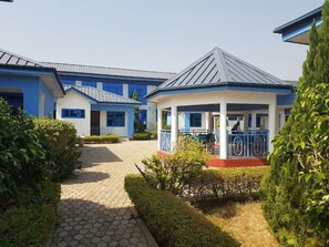 A building with a covered outdoor area, paved pathways, and neatly trimmed bushes. - Blue Hill Hotel (Bamahu)