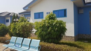 A building with a blue and white exterior, a bench with a water bottle, and a large bush in front. - Blue Hill Hotel (Bamahu)