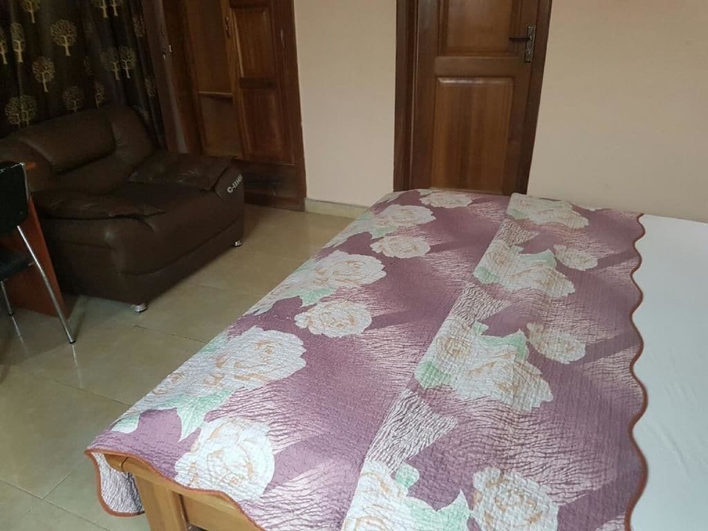 A bedroom with a bed covered in a floral-patterned bedspread, a brown leather sofa, and a wooden door.