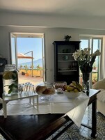 Un comedor con una mesa preparada para dos, un jarrón de flores blancas y vistas al exterior.