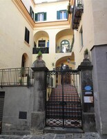 Un patio con entrada porticada, pilares de piedra y una escalera que lleva a un nivel superior.