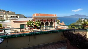 A balcony with potted plants, a view of the sea, and a mountain in the distance. - Vesuvio View (Vico Equense)