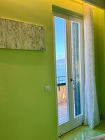 Una habitación con pared verde, una puerta que da a un balcón y una obra de arte abstracta.